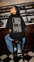 Person wearing a black t-shirt, collingwood sport merch, sitting on a stool in a bar setting.